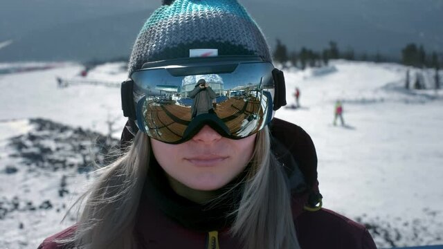 A beautiful girl puts on winter goggles or a mask for snowboarding. The concept of victory in sports, winning, win. Getting ready for skiing on a snowy slope. Winter travel at the ski resort.