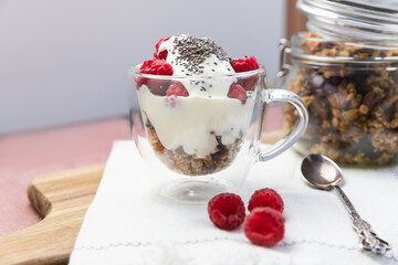 Granola in a jar and in a cup with yogurt and raspberry. Granola is a breakfast food and snack food consisting of rolled oats, nuts, honey, that is baked until golden brown