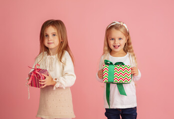 Giving and getting presents on Christmas holidays. Two little smiling children having fun, celebrating isolated on pink studio background. New Year 2021 meeting, childhood, happiness, emotions.