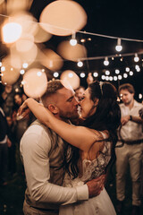 The bride and groom congratulate each other against the background of a flower arch. Evening wedding. Fireworks and lights.