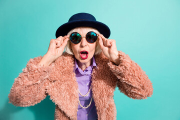 Photo of impressed old woman dressed vintage outerwear cap arms eyewear isolated turquoise color...