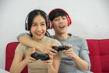 Couples play games and listen to sound through bluetooth headphones and sitting on sofa at the...
