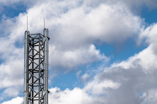 Shiny metal chimney with lightning rods against the background of a blue sky with clouds.