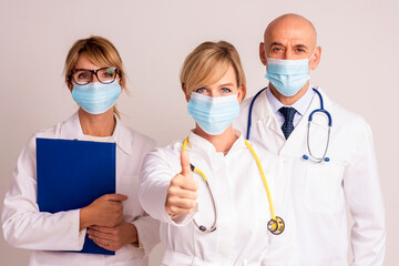 Female medical worker wearing face mask and giving thumbs up while standing together with her...