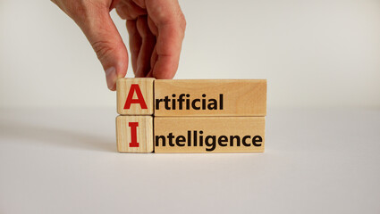 Wooden blocks and cubes with the text 'AI - artificial intelligence' on beautiful white background. Male hand. Business concept, copy space.