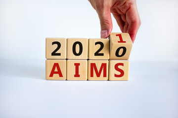 Business concept of planning 2021. Male hand flips a wooden cube and changes the inscription 'Aims 2020' to 'Aims 2021'. Beautiful white background, copy space.