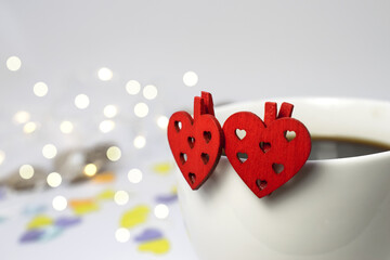Two red wooden hearts hang on a white coffee Cup on a white background with bokeh. Holiday background. Valentine's day