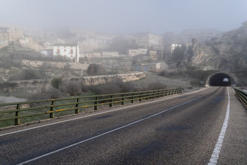 Pueblo de Sepulveda en un día de invierno frío y con mucha niebla. Carretera vacía que lleva a un tunel debajo de montaña.