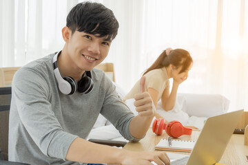 Obraz na płótnie Canvas A good looking asian man work on his desk. young man was successful career. His job is sell online, with a girlfriend sitting in bed assistant to work