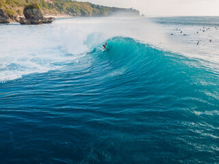 Aerial view with surfing at barrel wave. Blue perfect waves and surfer