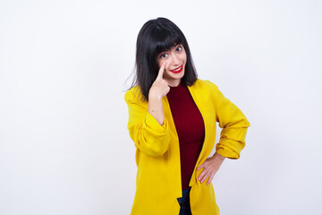 Caucasian woman standing against white background wearing yellow blazer, looking, observing, keeping an eye on an object in front, or watching out for something.
