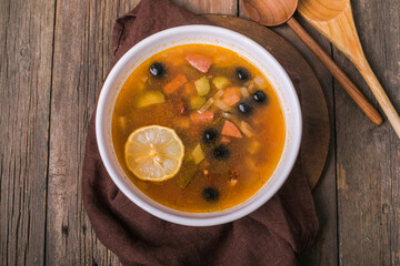 Slavic Solyanka soup in a white bowl on dark wooden background with copy space. Top view. Famous traditional Ukrainian and Russian saltwort soup with lemon.