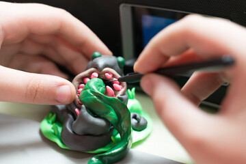 The hands of a child with modeling utensils are manipulating polymer clay to create a figure that...