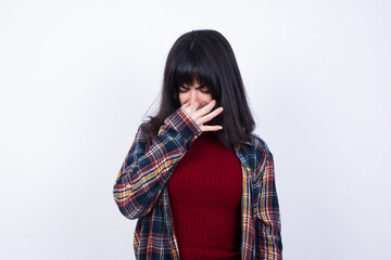 Beautiful young Caucasian woman standing against white background, holding his nose because of a bad smell.