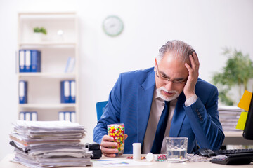 Old male sick employee working overtime in the office