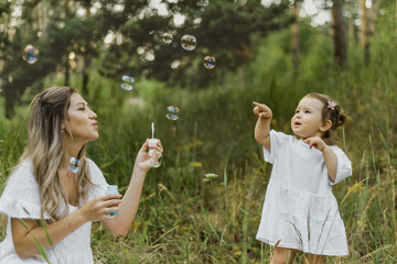 a mother blows soap bubbles for a child in the Park. a mother plays with her daughter in nature. happy childhood