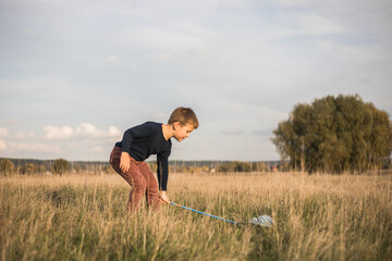 Naklejka na ściany i meble Young boy with butterfly net walking meadow. Child playing catching insects. Seasonal summer activity for kids outdoor. Learning animal fauna world hobby.