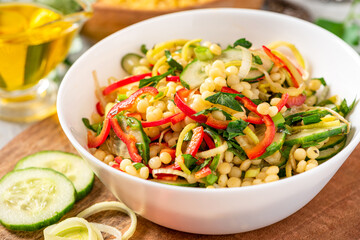 Vegetable salad with ptitim close-up. Salad made from toasted pasta ptitim (petit plomb or Israeli couscous), cucumbers, peppers, onions, and parsley. Vegan food. Mediterranean and Israeli cuisine.