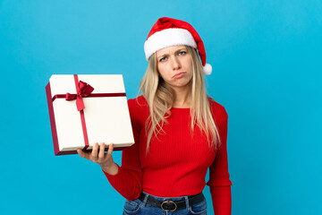 Fototapeta na wymiar Woman with christmas hat holding a present isolated on blue background with sad expression
