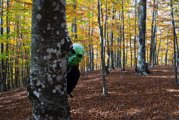 alien woman hides behind a tree in the autumn forest