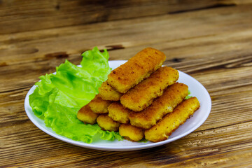 Fried fish fingers on a plate with lettuce on wooden table