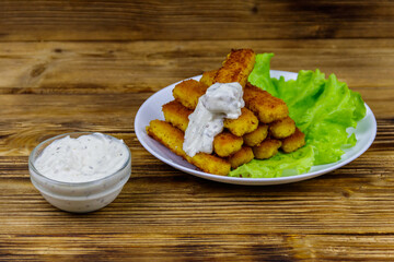 Fried fish fingers on a plate with lettuce and tartar sauce on wooden table