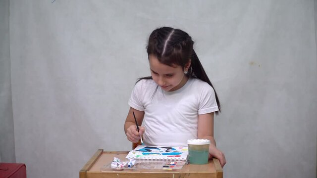 A cute girl draws a multicolored ornament on paper with acrylic paints and a brush.