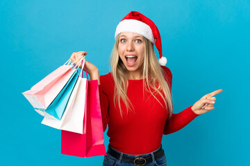 Obraz premium Woman with christmas hat going to buy something isolated on blue background surprised and pointing finger to the side