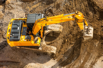 Obraz premium Excavator on the ground of a construction site with a raised bucket, top aerial view.