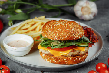 Turkey burger on a bun with cheese, lettuce, tomatoes and fresh cucumber. Burger with cutlet of turkey meat on a gray background with french fries