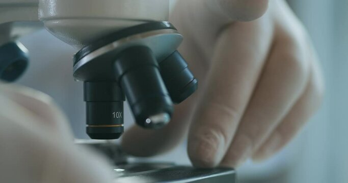 Close up of microscope oculars being directed at a sample on a piece of glass. Close-up shot of sample slide and microscope with metal lens at laboratory.