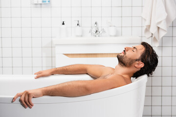 Bearded man taking bath with closed eyes at home - Powered by Adobe