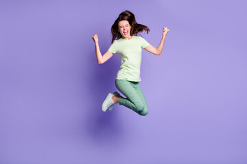 Fototapeta na wymiar Photo portrait full body view of cheerful girl celebrating victory with raised fists jumping up isolated on vivid violet colored background