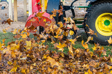 a tractor with a blower cleans a city park lawn and blows away autumn leaves, close-up