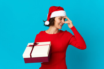 English girl with christmas hat holding a present isolated on blue background laughing