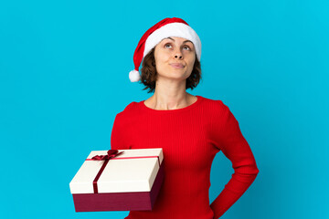 English girl with christmas hat holding a present isolated on blue background and looking up