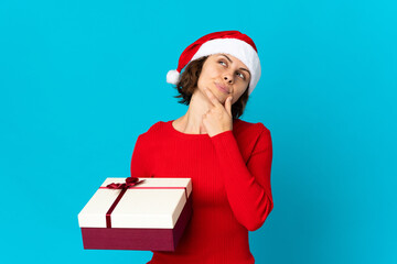 English girl with christmas hat holding a present isolated on blue background and looking up