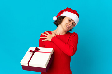 English girl with christmas hat holding a present isolated on blue background suffering from pain in shoulder for having made an effort