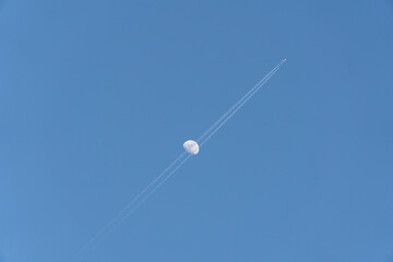 昼間の月に重なる飛行機雲