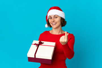 English girl with christmas hat holding a present isolated on blue background making money gesture