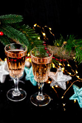 New Year and Christmas decor. Glasses for champagne, toys for the Christmas tree stand on the table in front in the dark, beautiful bokeh on the background. Close-up, top view.