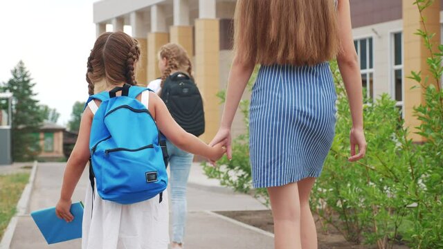 parent leads to school child with backpack back view. kids go to school with backpacks education concept. mom leads daughter by hand to first lesson. group school lifestyle girl children go to class
