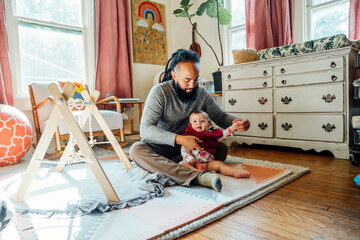 Dad sitting on floor of nursery dressing baby