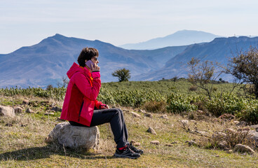 Naklejka na ściany i meble Young woman in red mountain clothes, talking on her cell phone and contemplating the valley