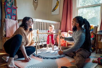 Happy mom and dad playin with baby in sunlight filled nursery