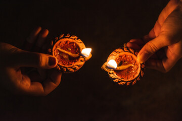Close up shot of hands of two woman holding lit diya during Indian festival Diwali