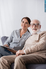 happy woman with laptop and aged father looking at camera on blurred foreground