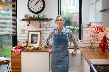 Blond woman wearing blue apron standing in kitchen, smiling at camera.