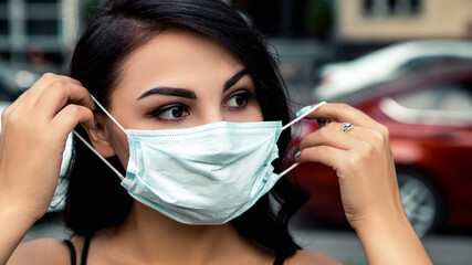 Young pretty lovely woman small business owner standing on the street car cafe restaurant and wear face disposable blue mask to prevent disease corona virus, looking at the camera. Healthcare concept.