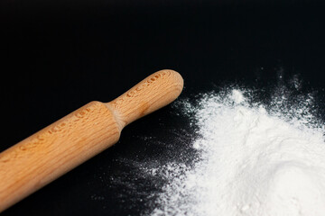 At the bottom of the screen, on the dark surface of the table, there is a mound of white flour and a kitchen rolling pin.